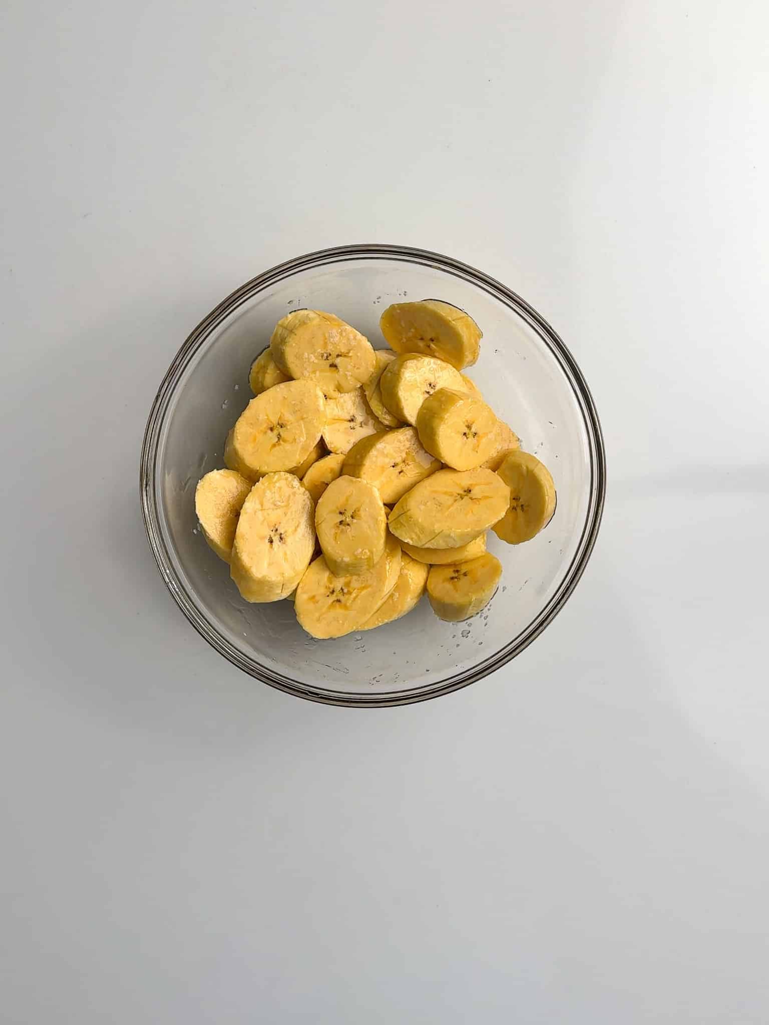Sliced plantains sit in a glass bowl before being seasoned.