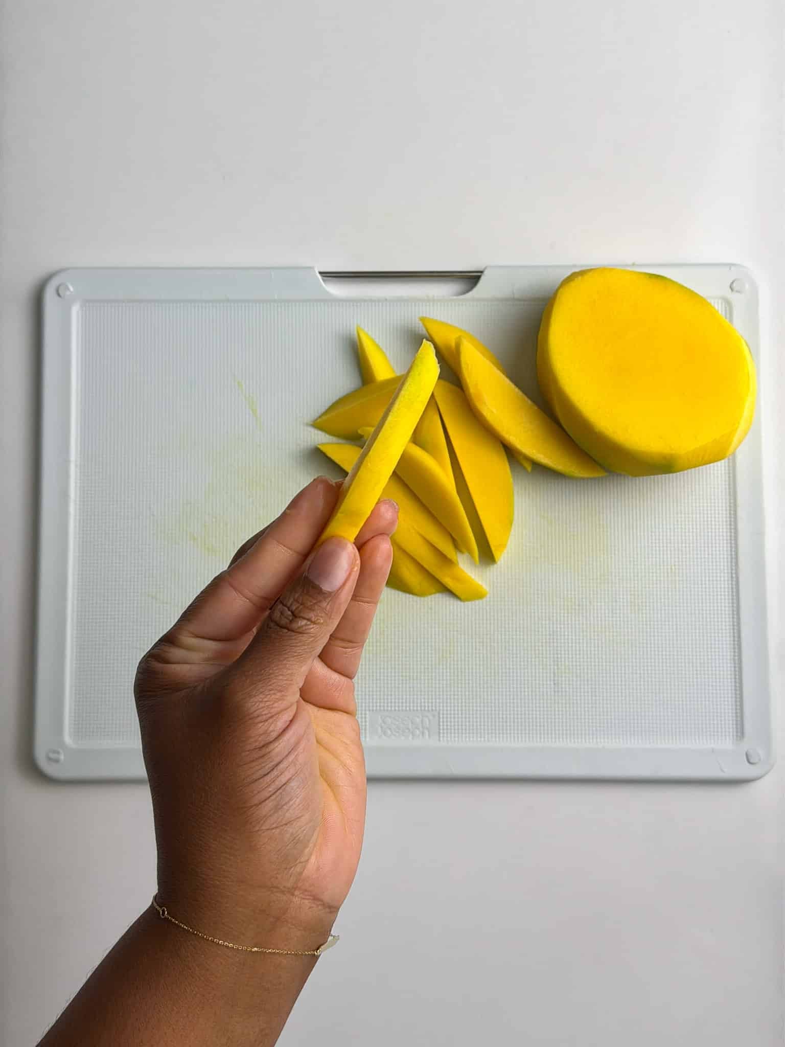 Close-up of hand holding sliced mango, showing how thick the slice is.