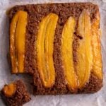 Overhead view of caramelized upside-down plantain bread with glossy plantain slices on top and one piece cut out.