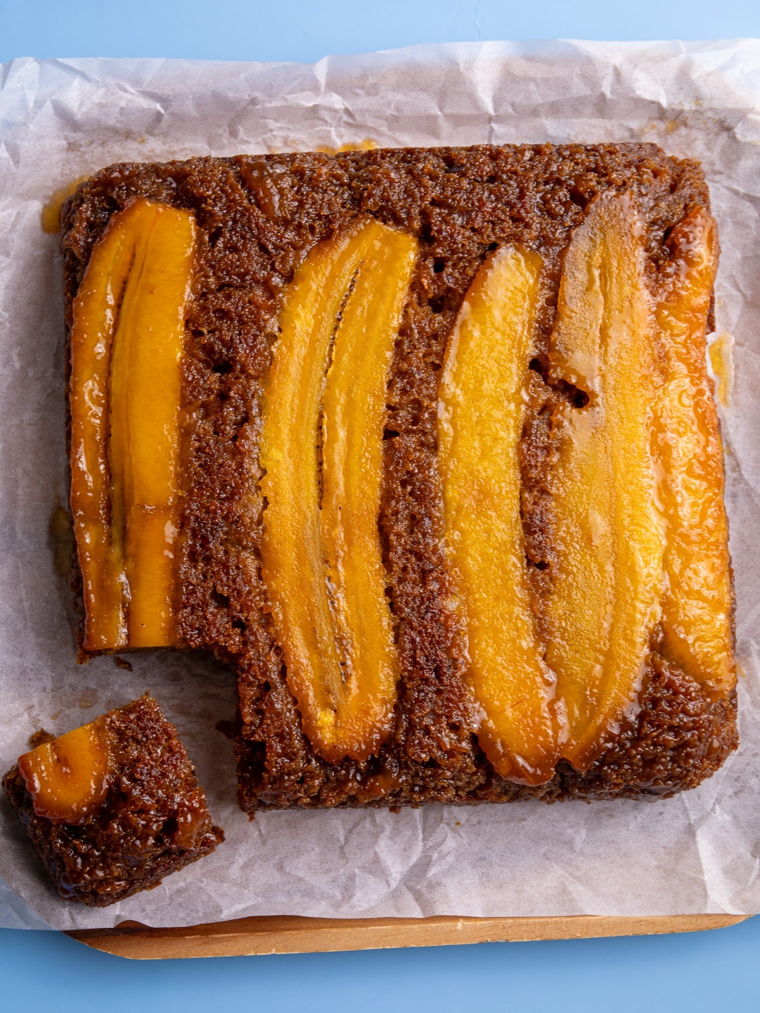 Overhead view of caramelized upside-down plantain bread with glossy plantain slices on top and one piece cut out.