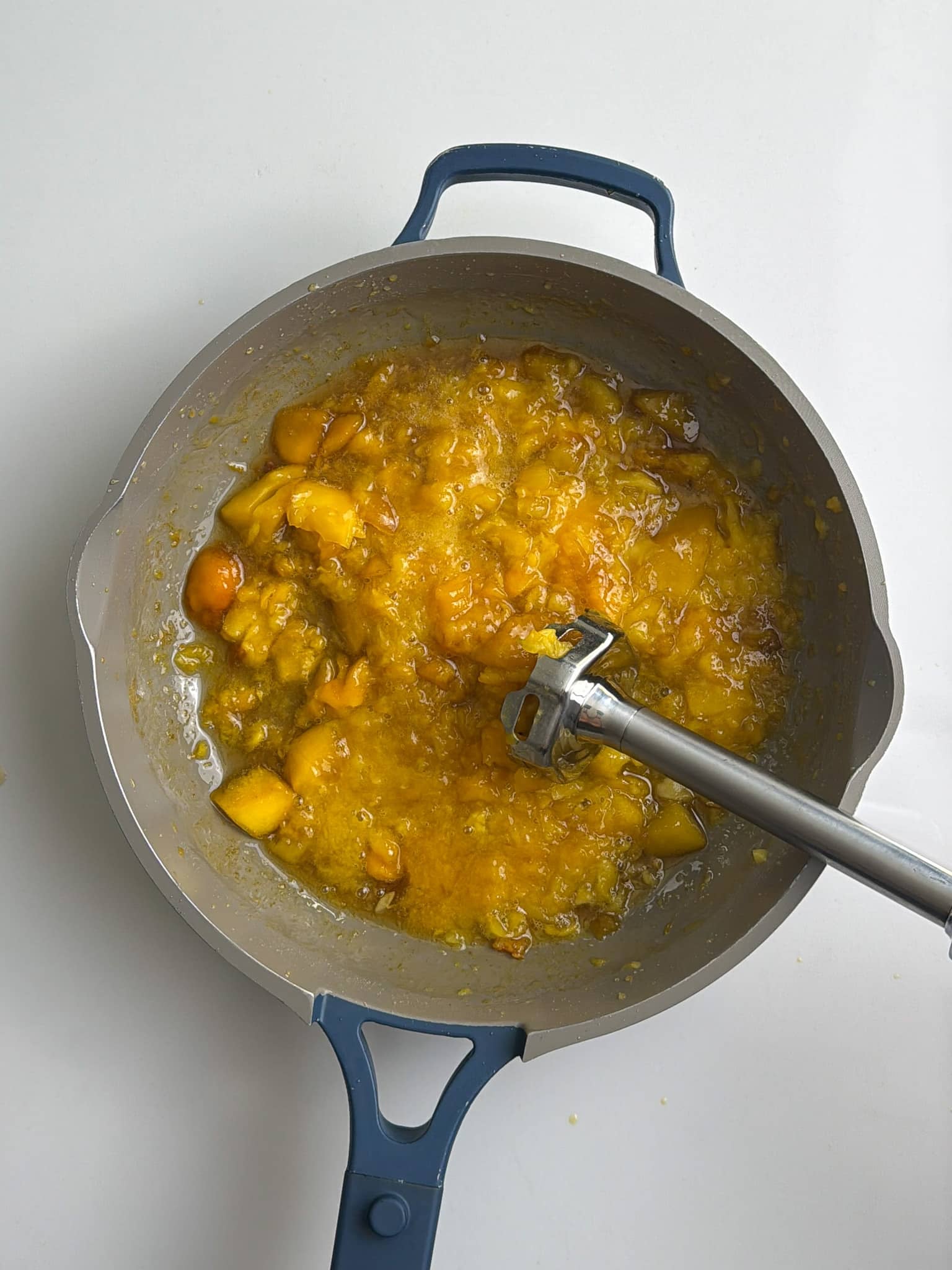 Diced mango cooking down in a saucepan while being stirred with a wooden spoon.
