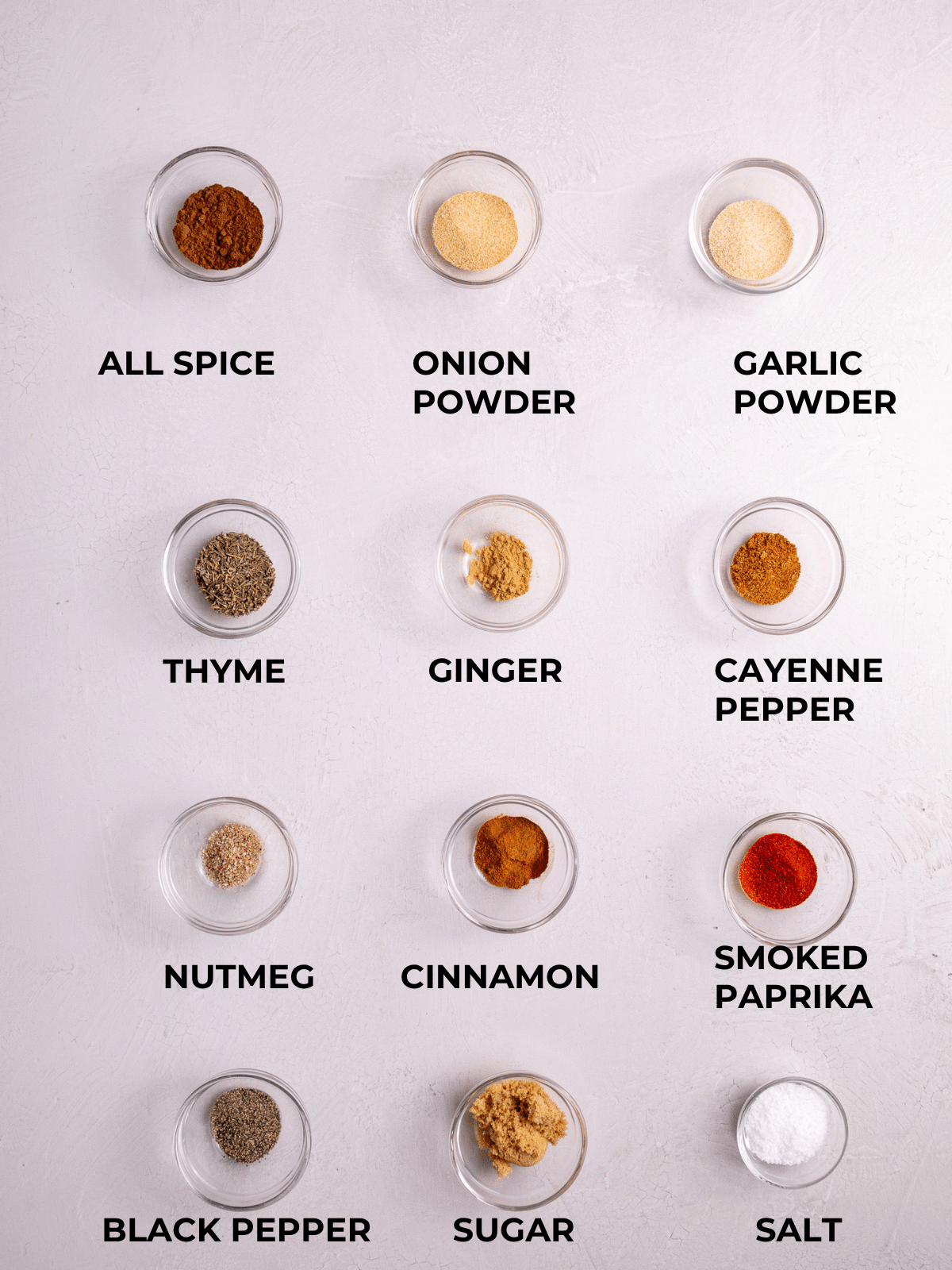Ingredients for homemade Jamaican jerk seasoning dry rub including allspice, thyme, smoked paprika, cayenne pepper, cinnamon, nutmeg, garlic powder, onion powder, black pepper, salt, and sugar
