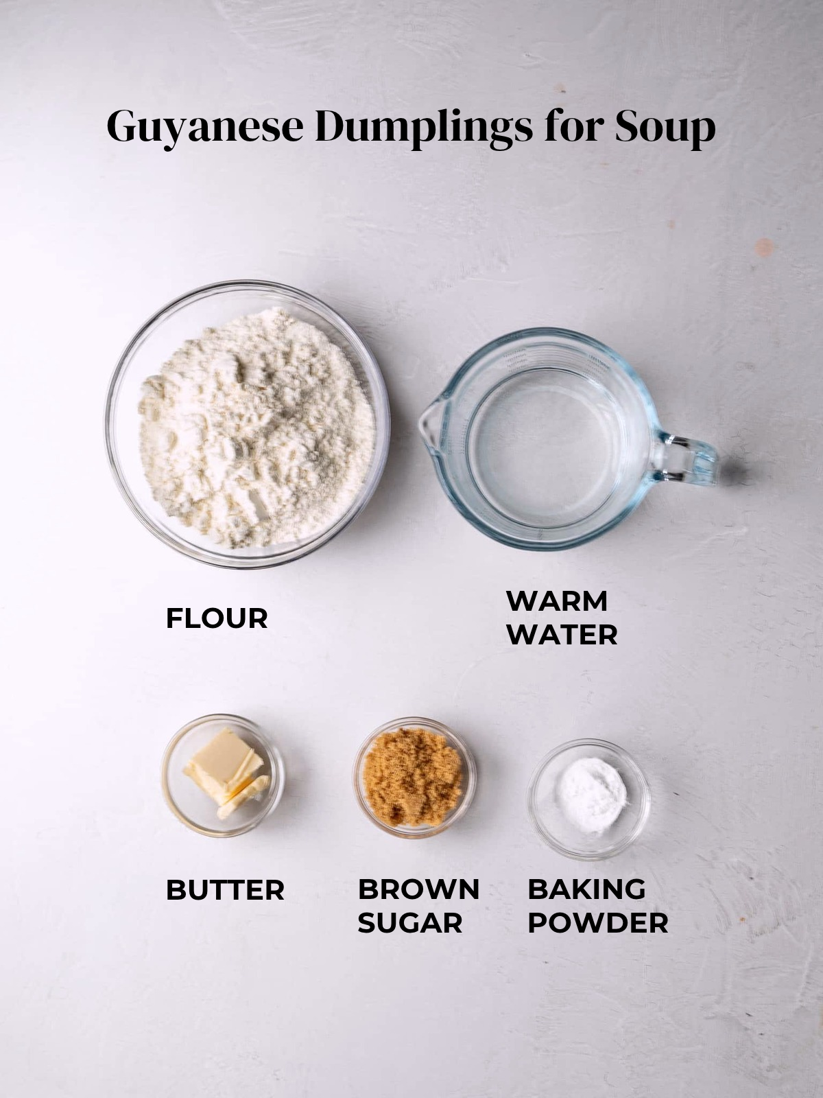 Labeled ingredients for Guyanese dumplings for soup in glass bowls: flour, warm water, butter, brown sugar, and baking powder