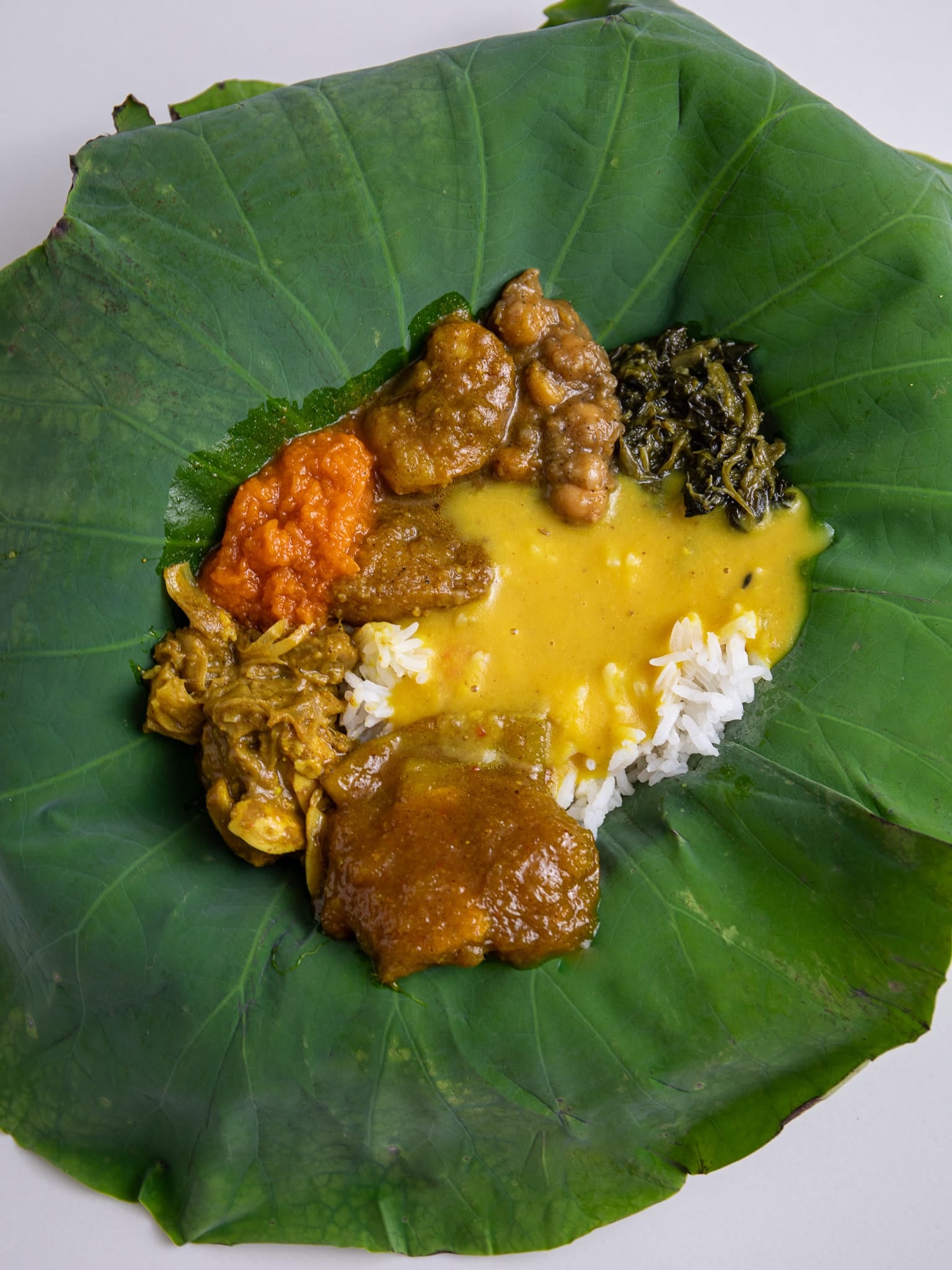 Guyanese seven curry on a lotus leaf: pumpkin, channa and aloo, bhaji, katahar, mango curry and baigan around white rice